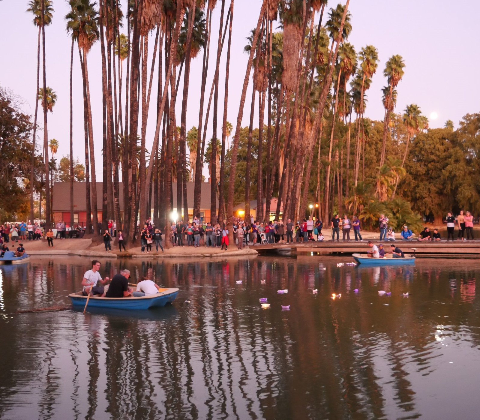 People standing along shore of lake with boats in the water